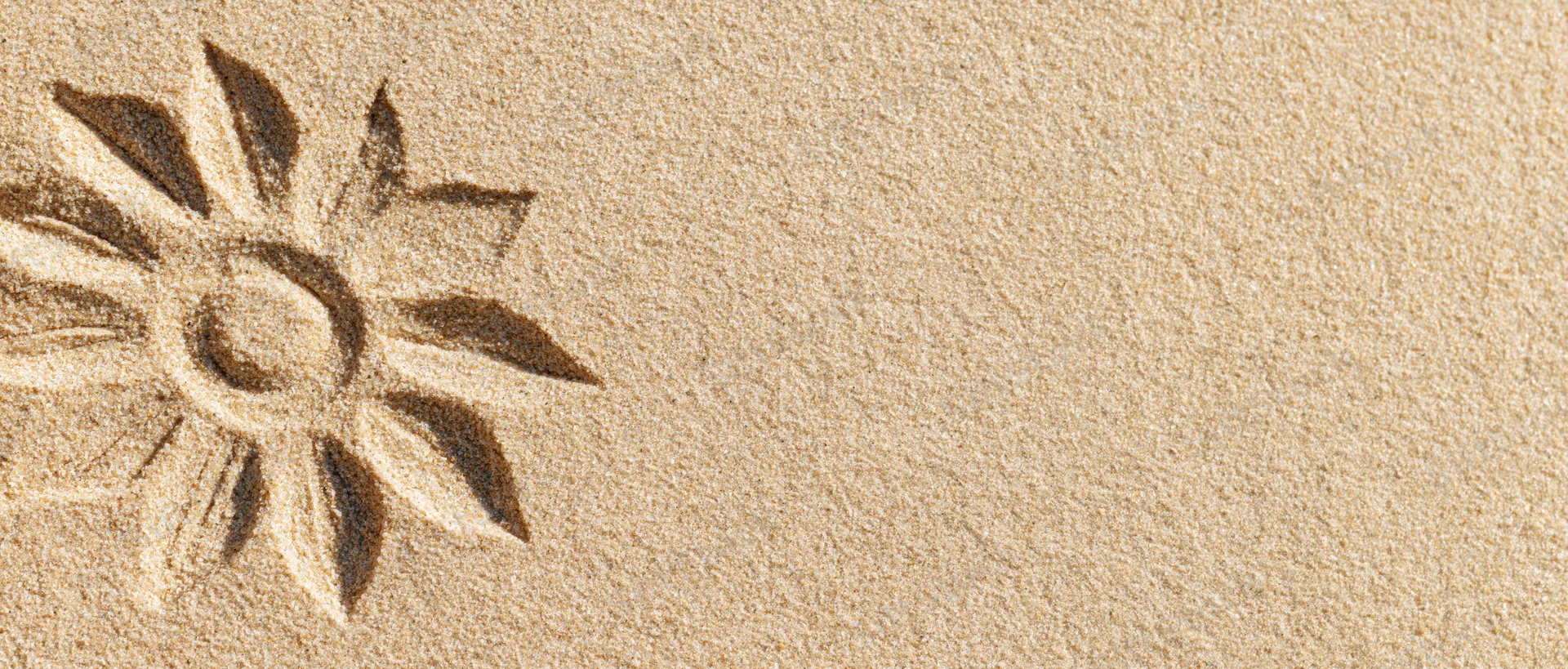 Sun shape drawn in dry beach sand with finger, simple petal design on textured surface