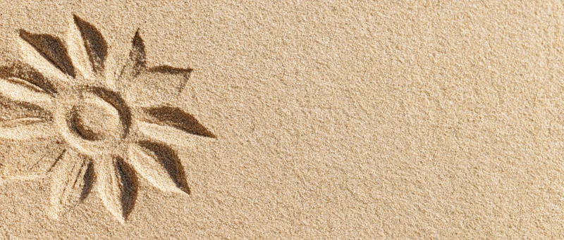 Sun shape drawn in dry beach sand with finger, simple petal design on textured surface