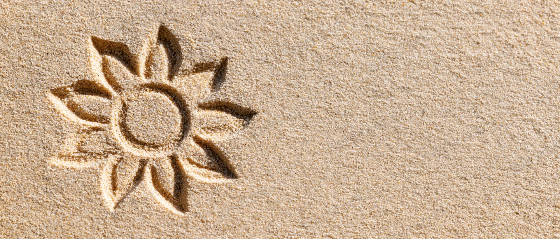 Sun shape drawn in dry beach sand with finger, left side of frame, copyspace on right