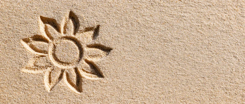 Sun shape drawn in dry beach sand with finger, left side of frame, copyspace on right