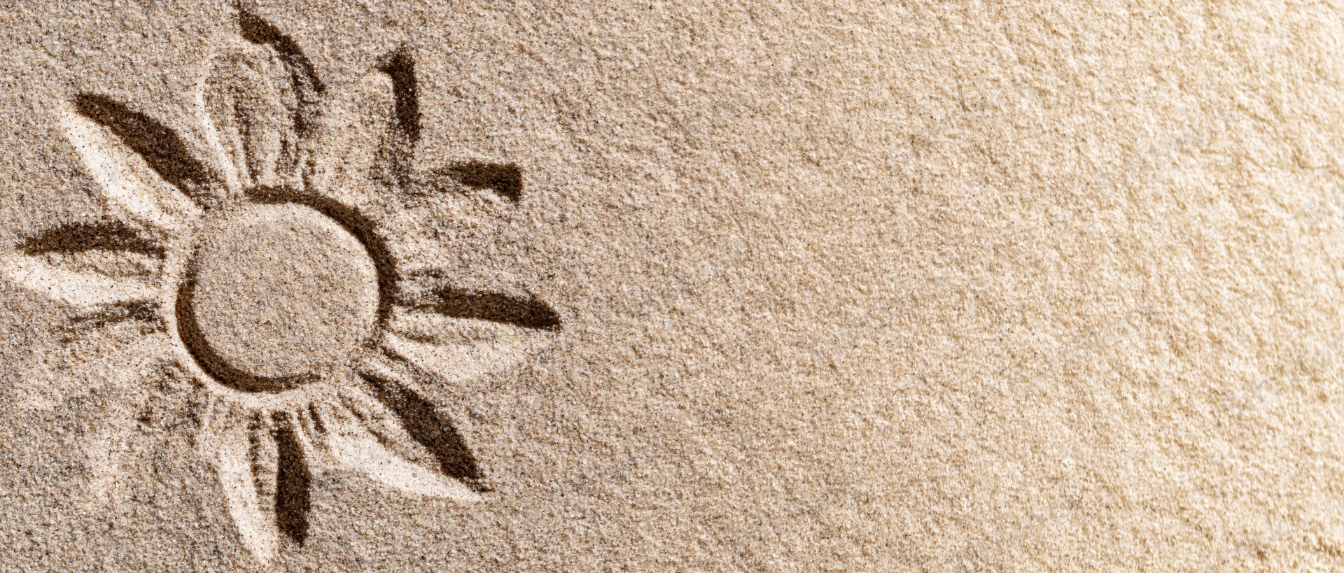 Sun shape drawn in dry beach sand with finger, left side of frame, copyspace on right