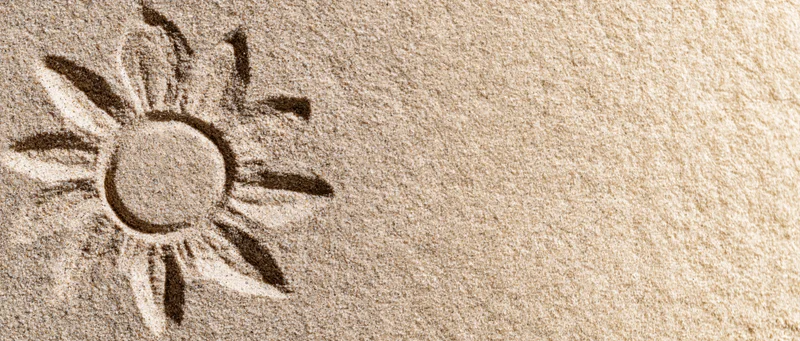 Sun shape drawn in dry beach sand with finger, left side of frame, copyspace on right