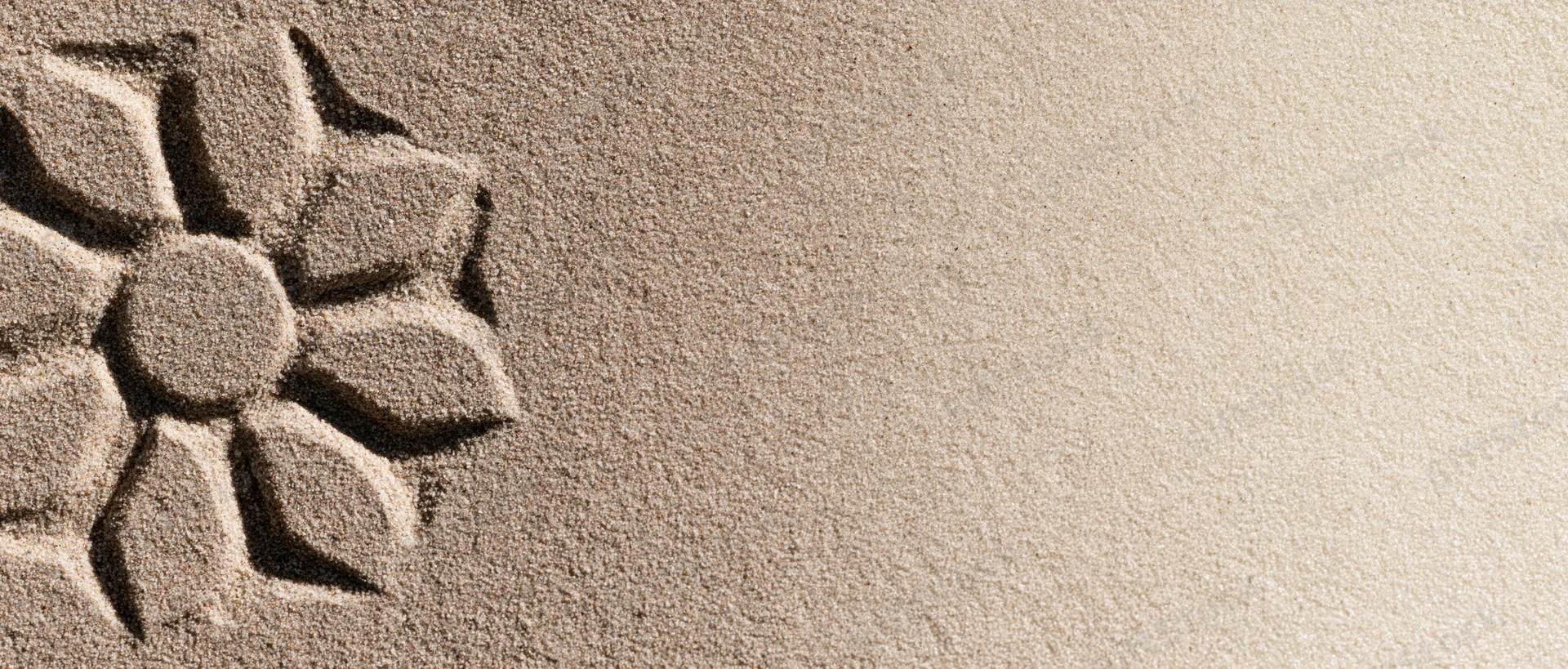 Sun-shaped flower drawn in dry beach sand with finger, leaving textured imprint on the surface