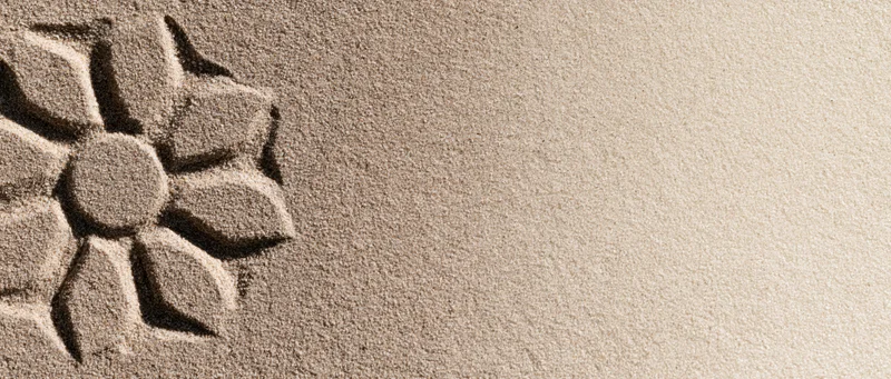 Sun-shaped flower drawn in dry beach sand with finger, leaving textured imprint on the surface