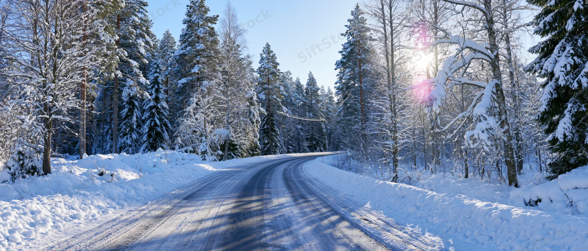 Curved rural road winding through snow-covered forest under bright winter sun