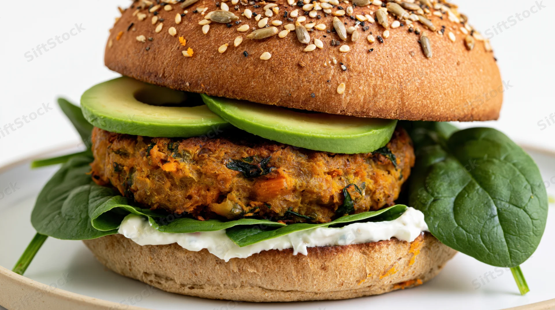 Veggie burger with avocado and spinach on a seeded bun served on a white plate