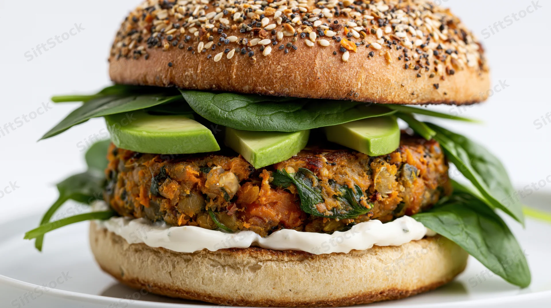 Veggie burger with avocado and spinach on a seeded brioche bun served on a white plate