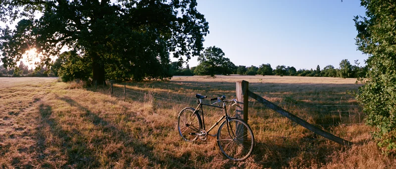 Vintage black bicycle leaning against wooden fence post in a sunlit rural field at golden hour