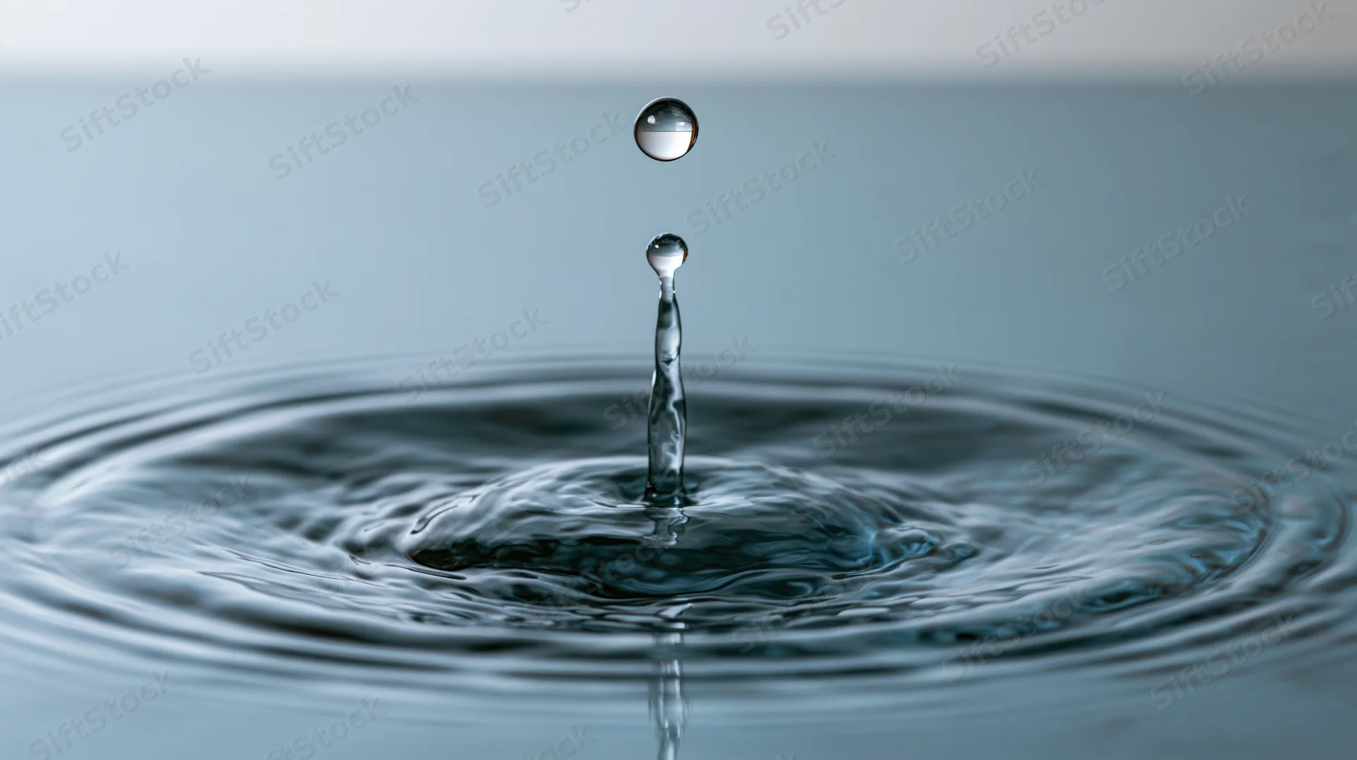 Water droplet mid-bounce above still surface creating ripples and reflection