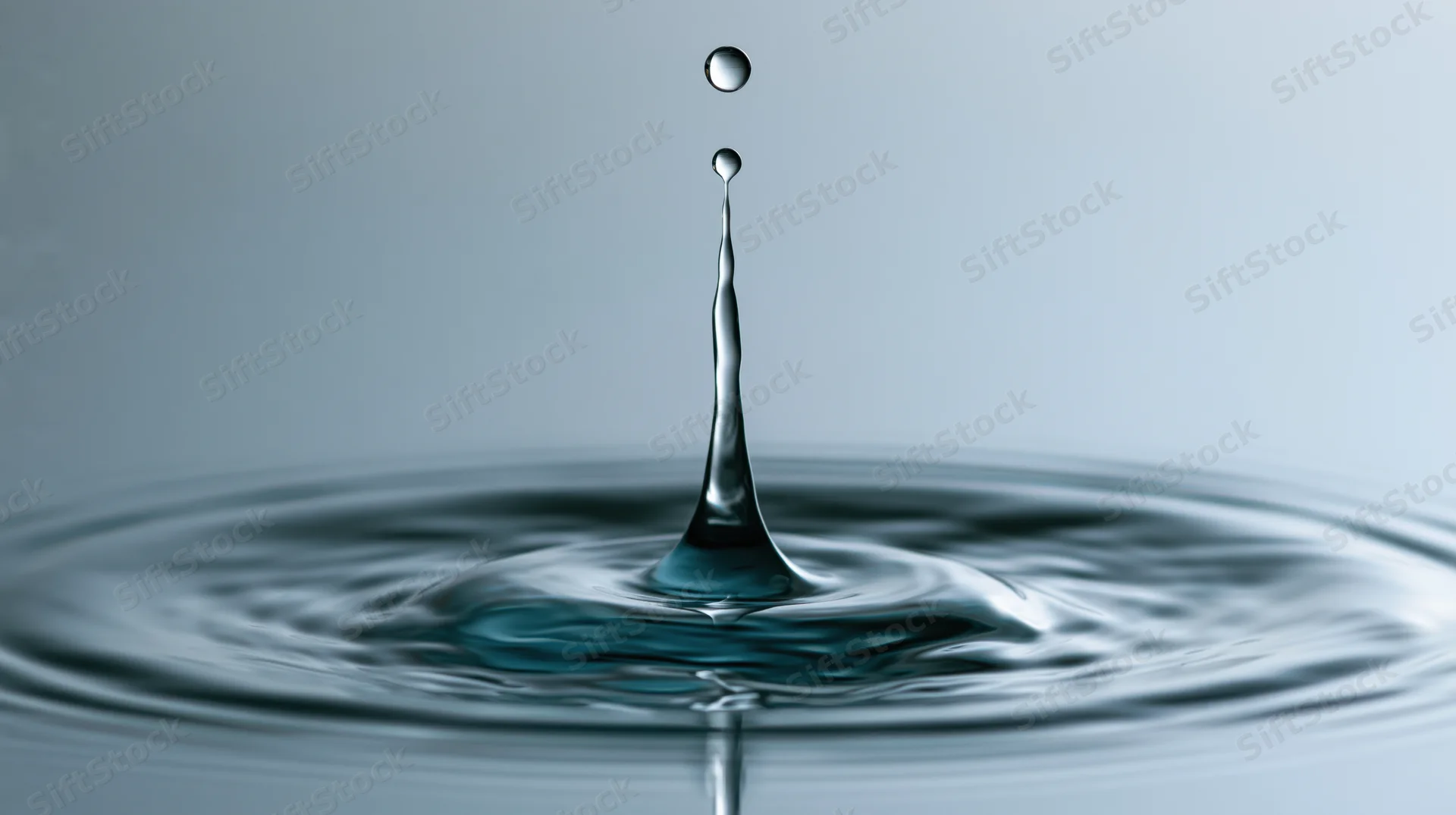 Water droplet mid-bounce above still surface creating crown splash and ripples