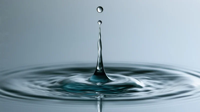Water droplet mid-bounce above still surface creating crown splash and ripples
