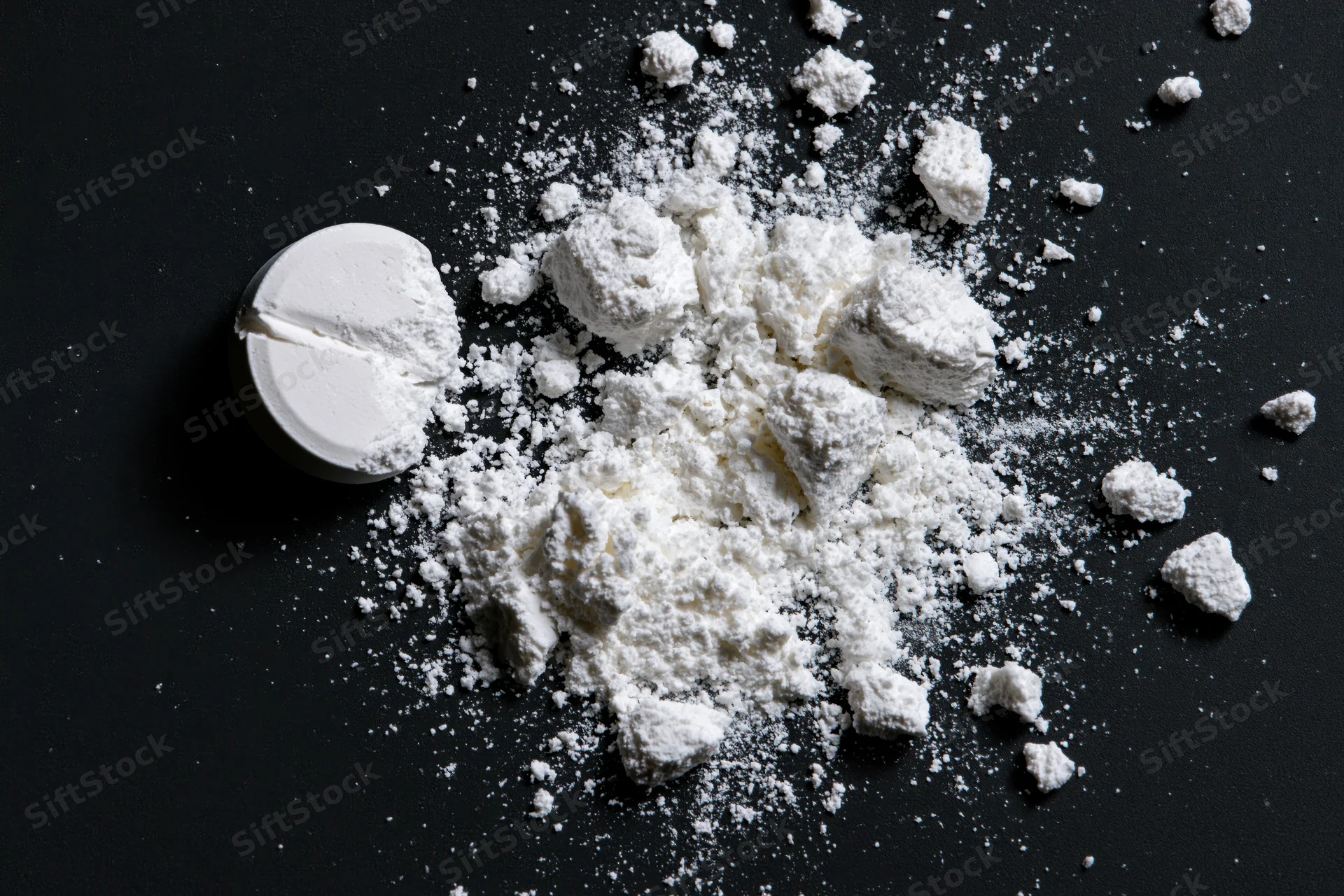 Crushed white pharmaceutical tablet scattered as powder on black surface