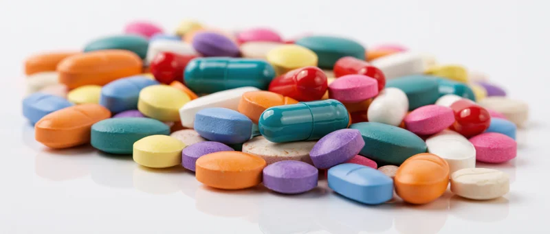 Scattered pile of colorful pharmaceutical pills and capsules on white reflective surface