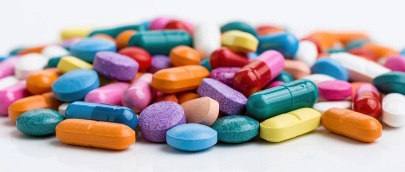 Scattered pile of colorful pharmaceutical pills and capsules on white surface