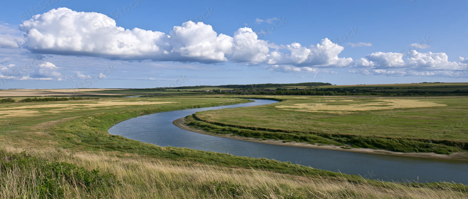 Winding river curving through open farmland under blue sky with clouds