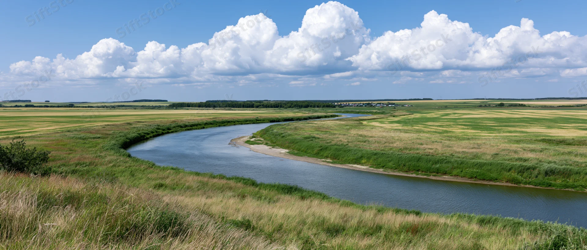 Winding river curving through open farmland under a blue sky with white clouds