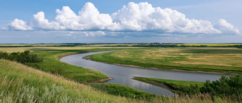 Winding river curving through open rolling farmland under a blue sky with white clouds