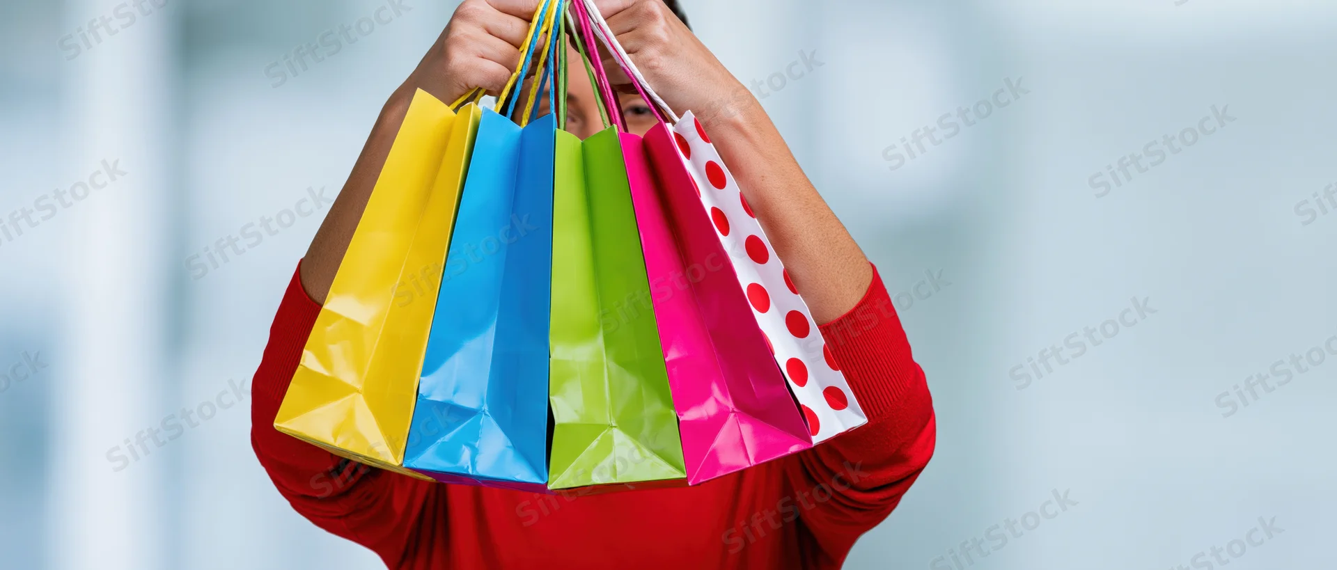 Woman holding multiple colorful paper shopping bags in front of her face