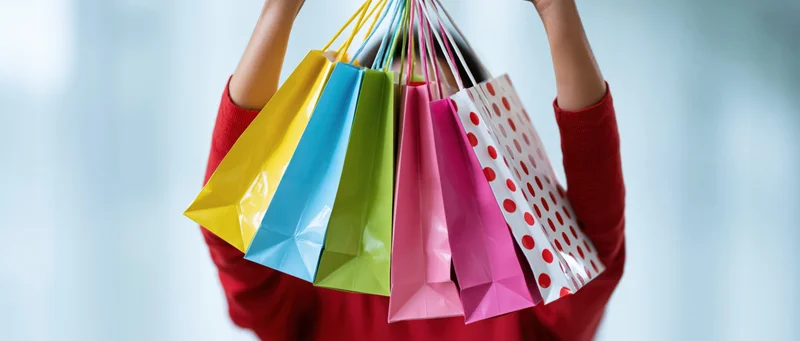 Woman holding multiple colorful paper shopping bags in front of her face