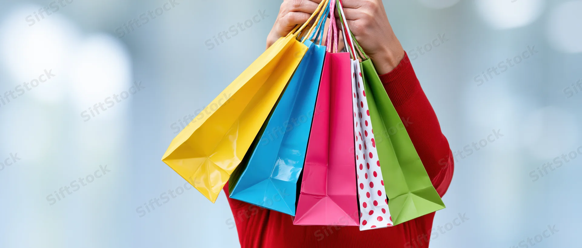 Woman holding multiple colorful paper shopping bags in front of her face