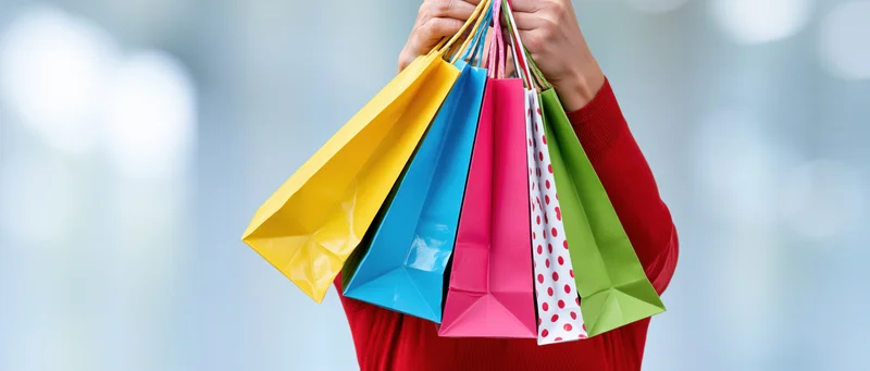Woman holding multiple colorful paper shopping bags in front of her face
