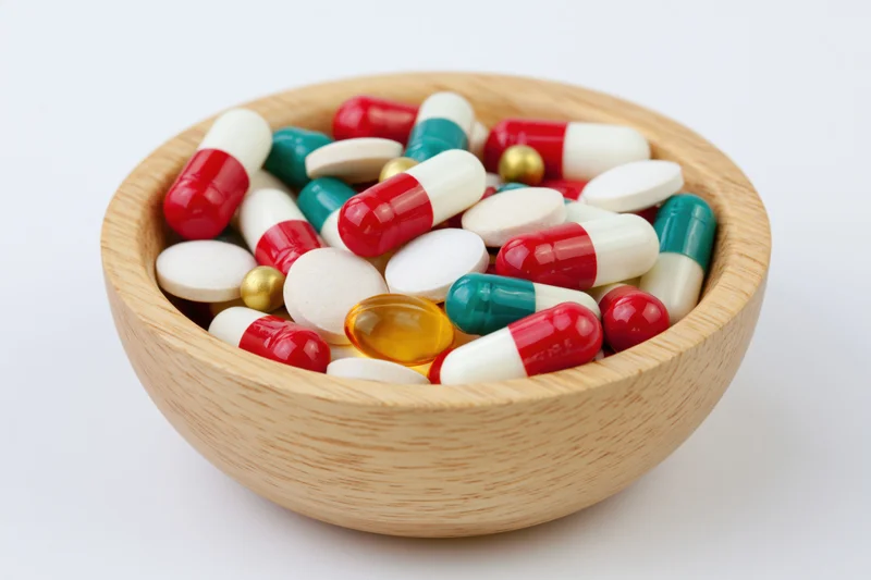 Wooden bowl filled with assorted pills and capsules on white background