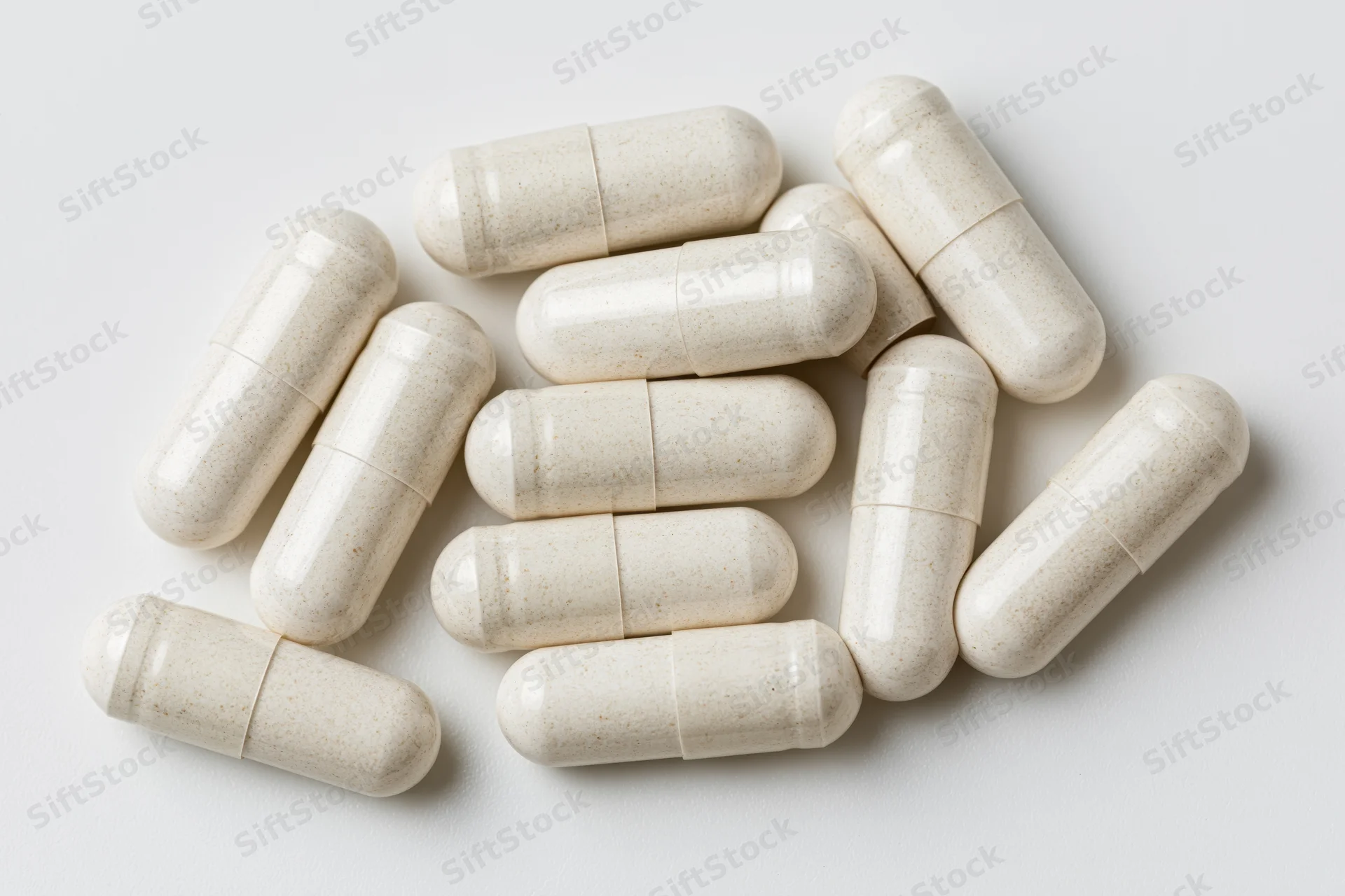 White gelatin supplement capsules scattered loosely on a plain white surface in a flat lay top view