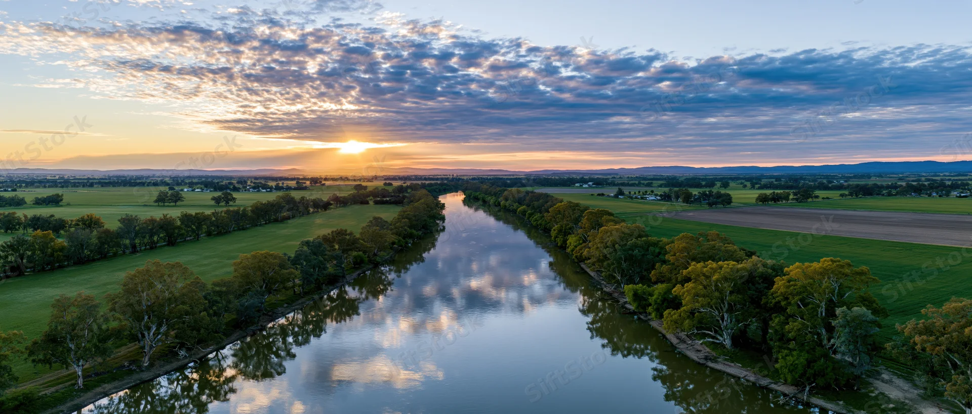 Aerial view of a river winding through green farmland at sunset in australia