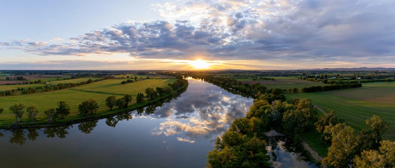 Aerial view of a river winding through green farmland at sunset with clouds reflected in the water
