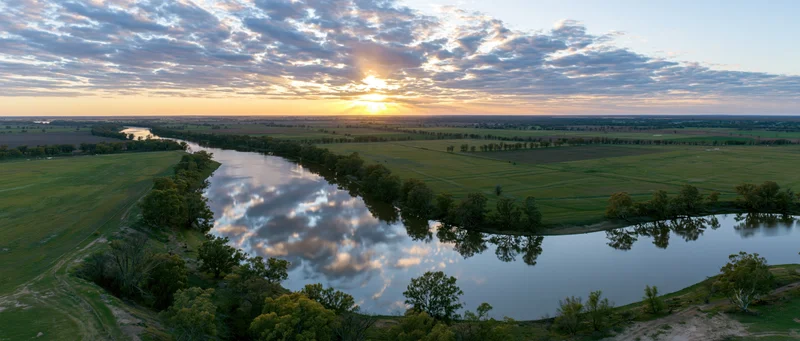 Aerial view of a winding river reflecting clouds at sunset over green farmland in australia