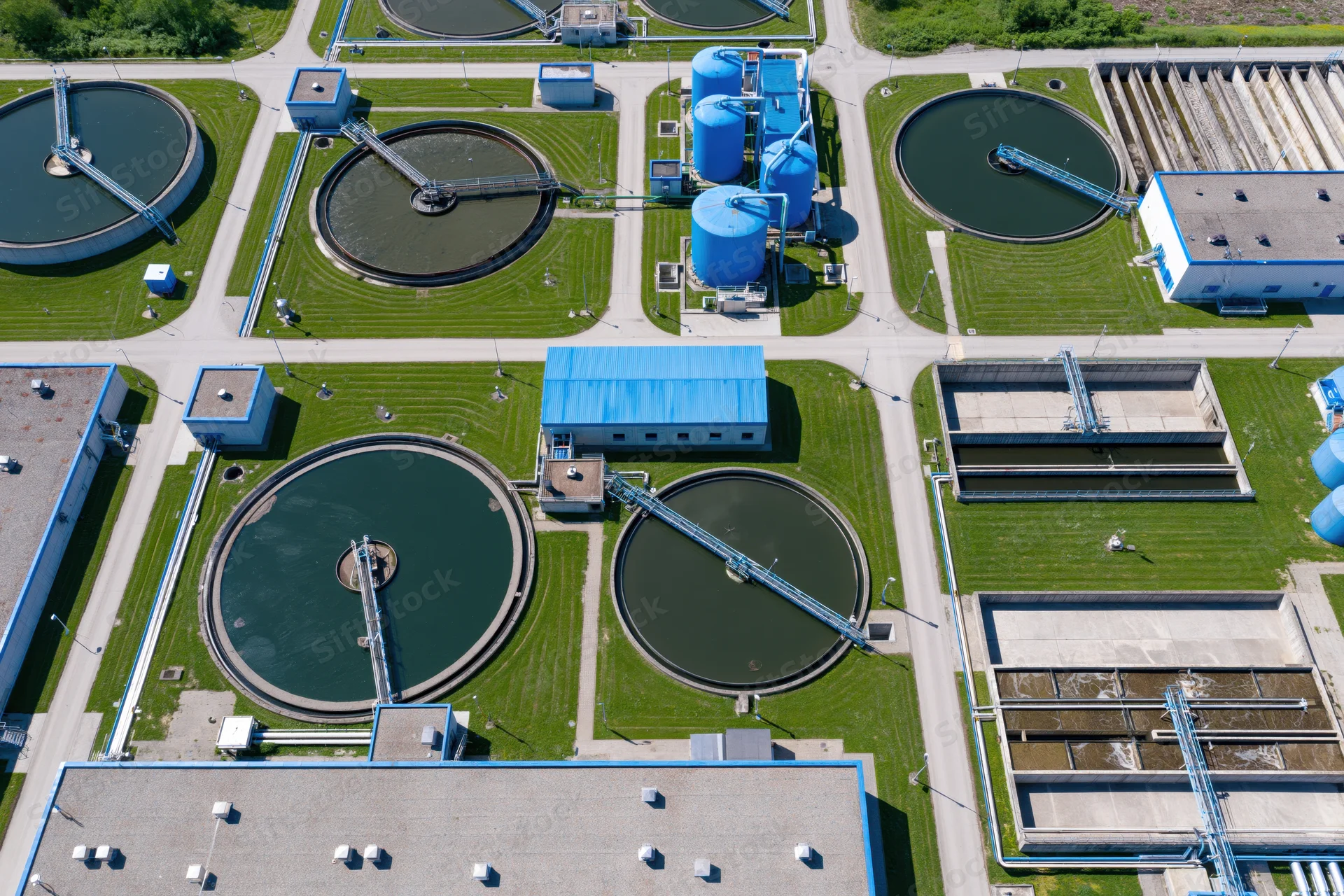 Aerial view of a large water treatment plant with circular tanks and blue buildings surrounded by green grass