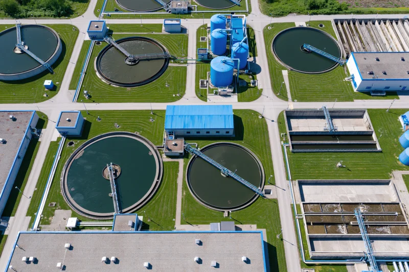 Aerial view of a large water treatment plant with circular tanks and blue buildings surrounded by green grass