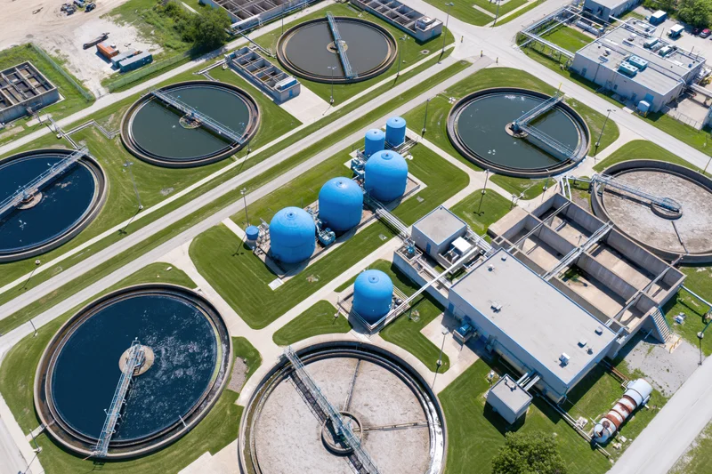 Aerial view of a water treatment plant with circular tanks and blue storage domes surrounded by green lawns and pathways