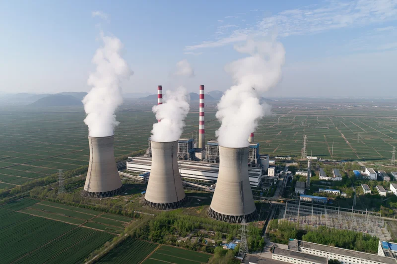 Aerial view of coal-fired power plant with cooling towers emitting steam over farmland