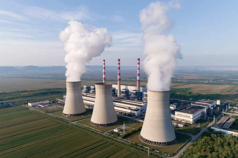 Aerial view of coal-fired power plant with cooling towers emitting steam over rural fields