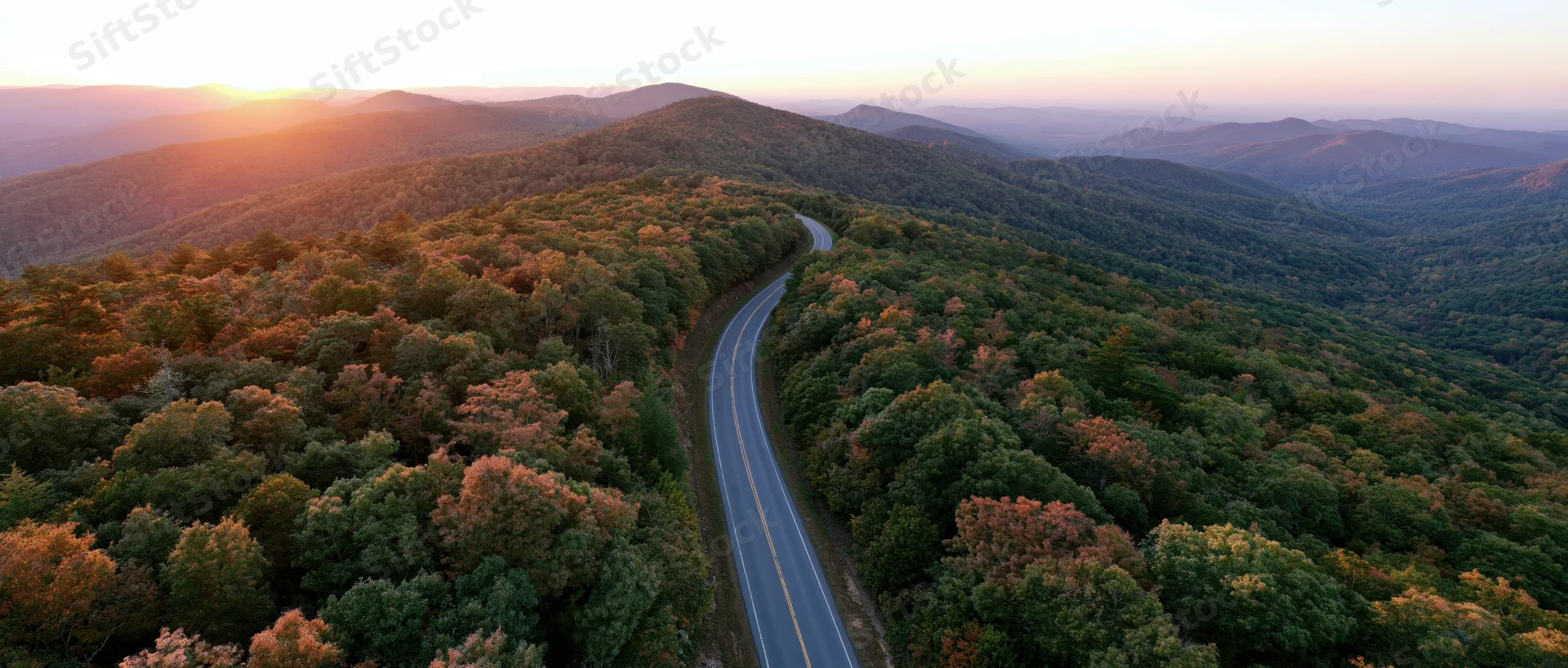 Aerial view of a winding road through autumn forested mountains at sunset