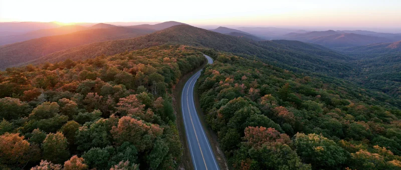 Aerial view of a winding road through autumn forested mountains at sunset