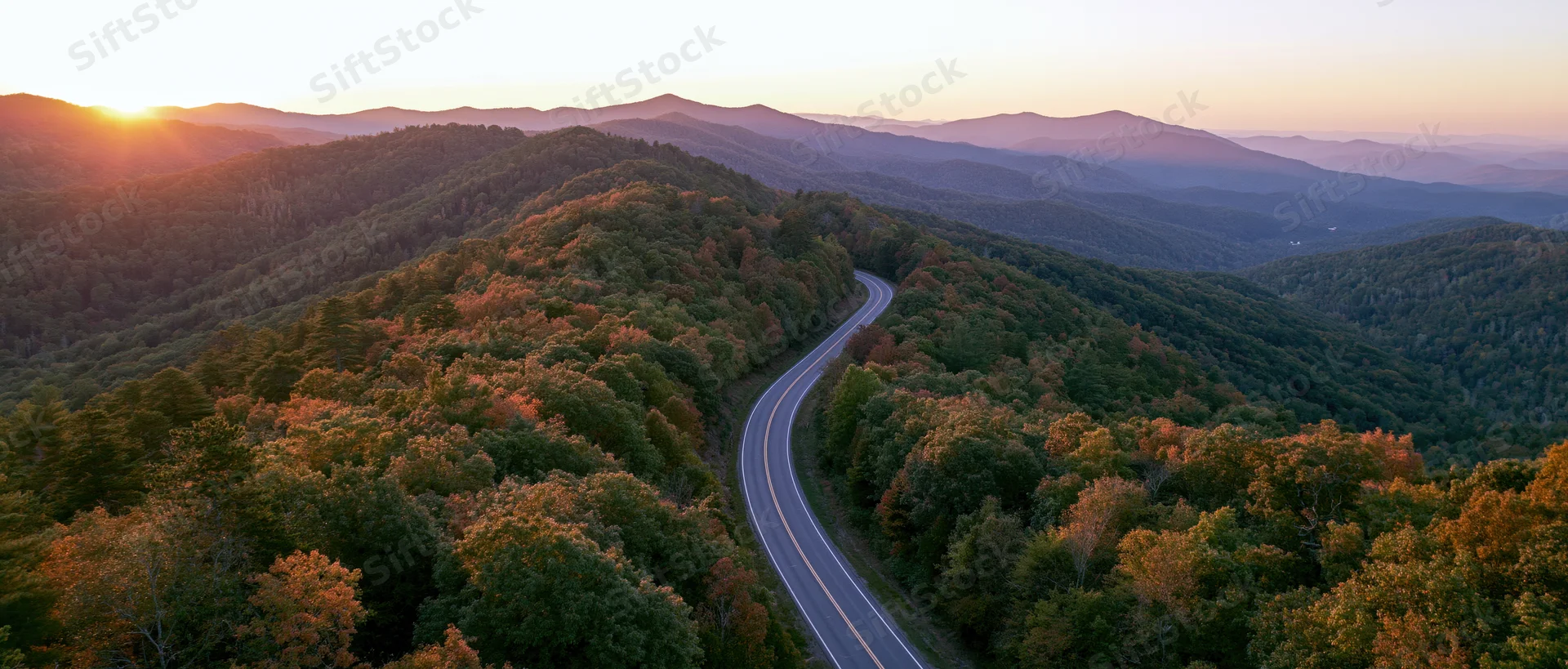 Aerial view of a winding road through autumn forested mountains at sunset