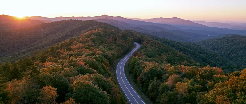 Aerial view of a winding road through autumn forested mountains at sunset