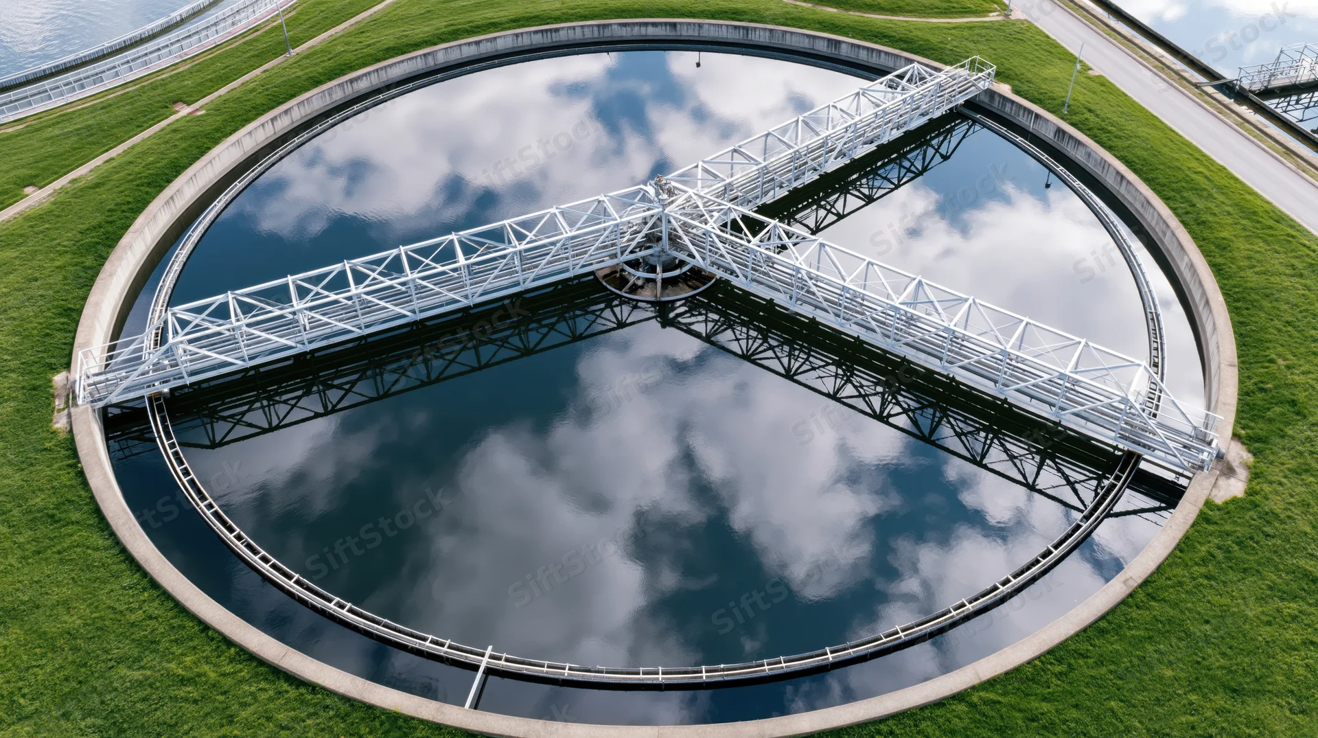 Aerial view of circular wastewater treatment clarifier tank with metal framework and sky reflection