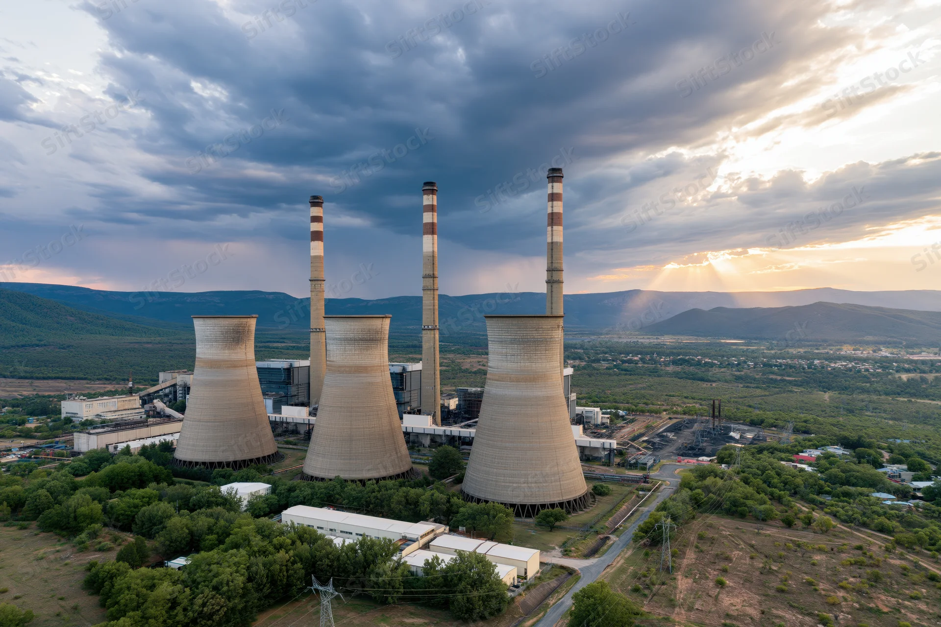 Aerial view of coal power plant with cooling towers and smokestacks at sunset over mountainous landscape