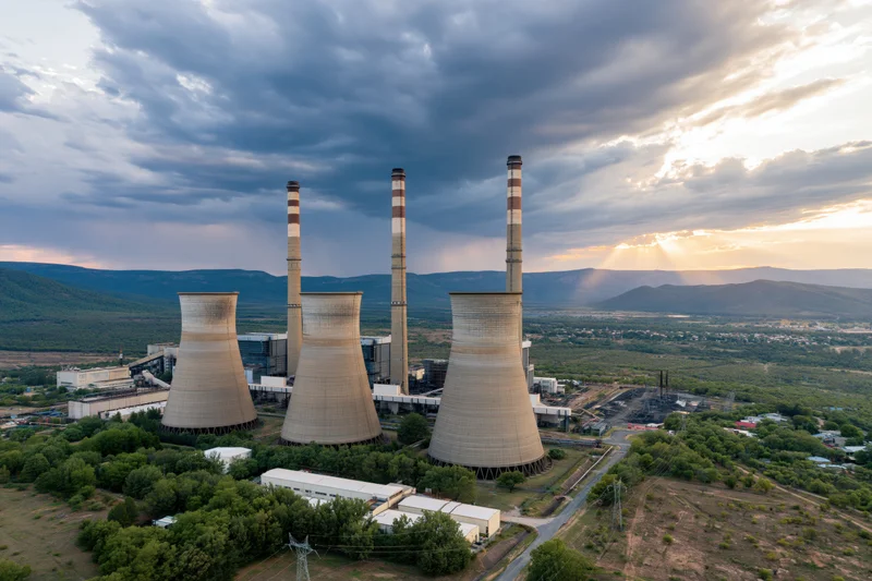 Aerial view of coal power plant with cooling towers and smokestacks at sunset over mountainous landscape