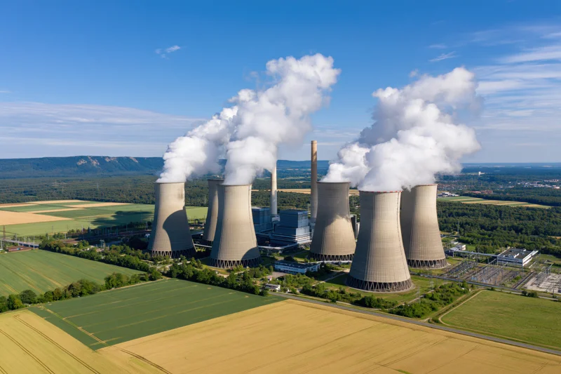 Aerial view of a coal-fired power plant with cooling towers emitting steam over farmland