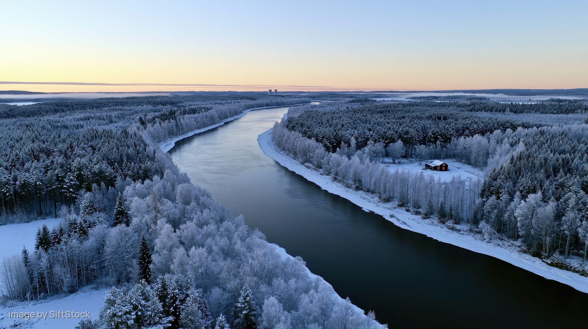 Wide river winding through snow-covered forest with red cabin at dawn
