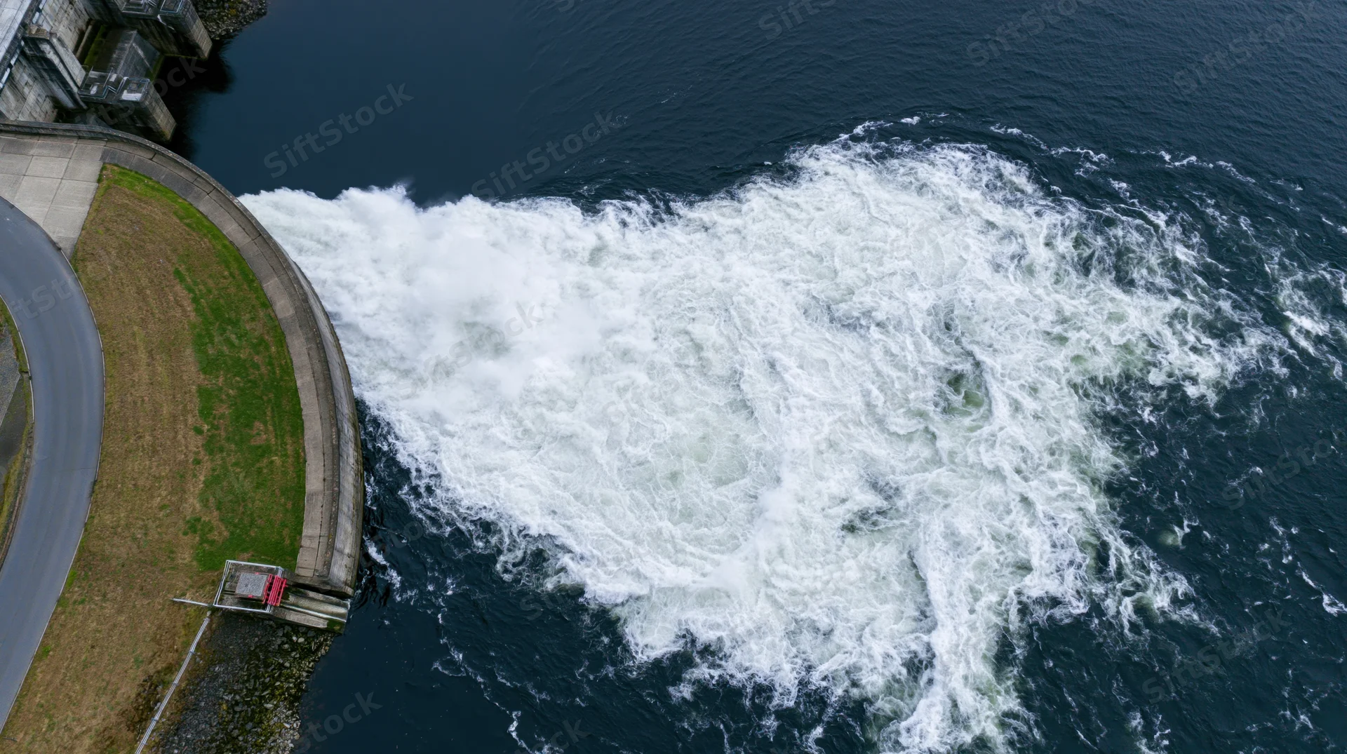 Aerial top-down view of dam spillway releasing turbulent water into river