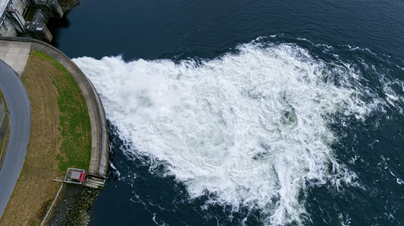 Aerial top-down view of dam spillway releasing turbulent water into river