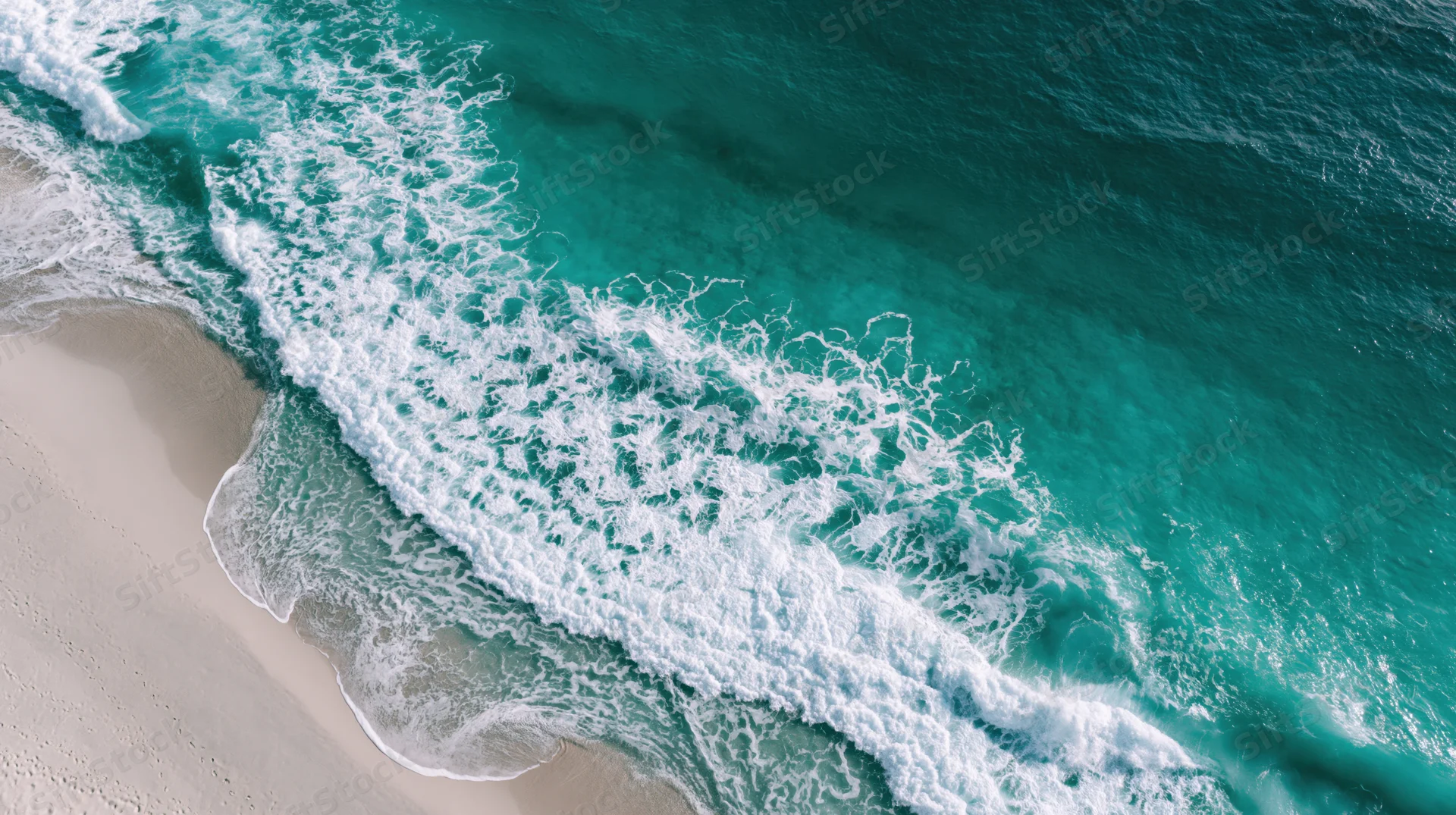 Aerial top-down view of turquoise ocean waves breaking onto a sandy beach