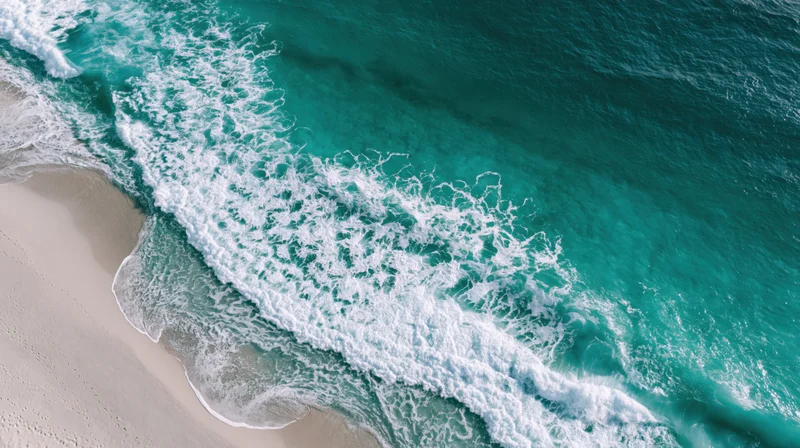 Aerial top-down view of turquoise ocean waves breaking onto a sandy beach