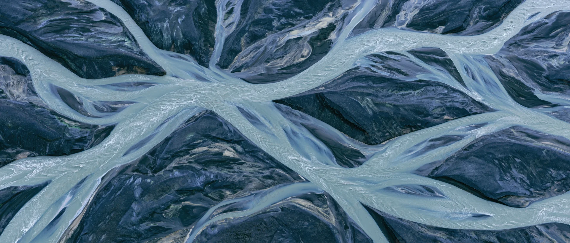 Aerial top-down view of a braided glacial river delta flowing through rocky terrain