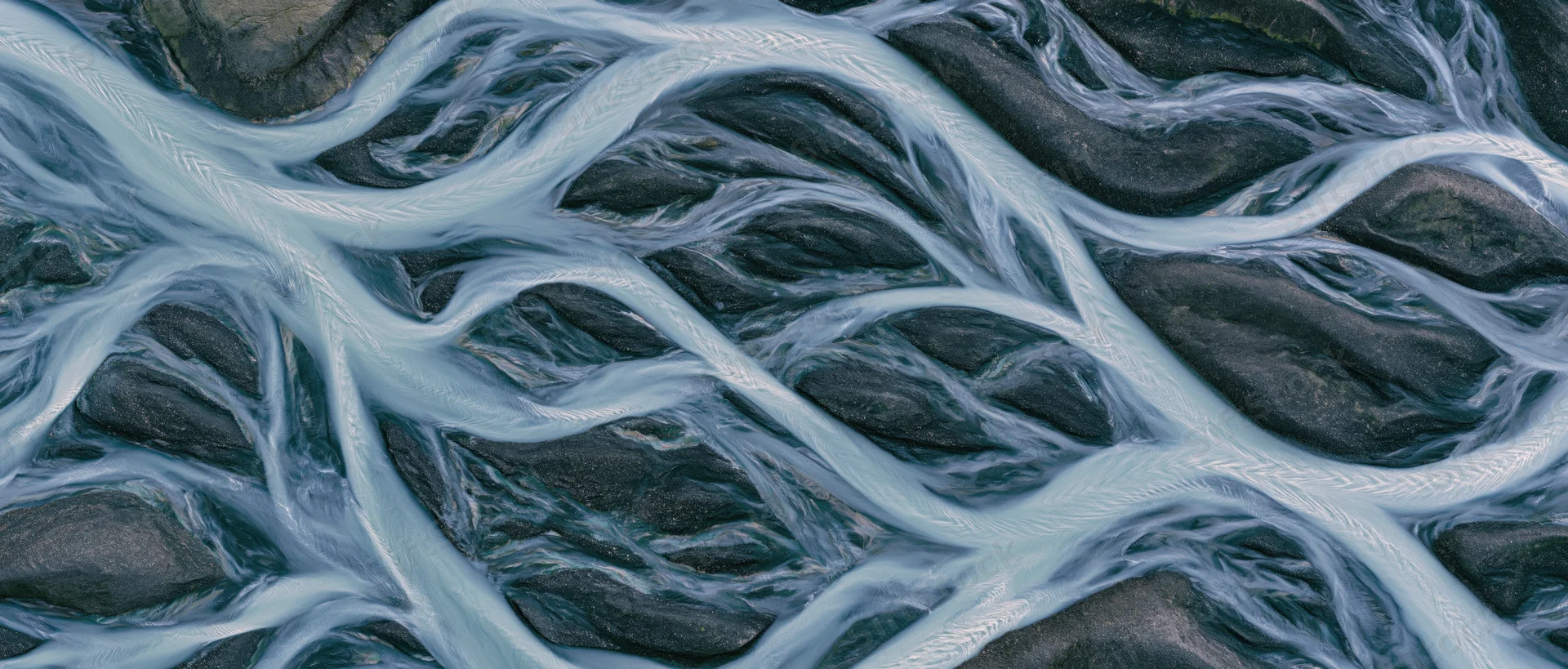 Aerial top-down view of a braided glacial river delta flowing over dark rocky terrain in Iceland